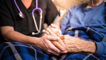 Palliativpflegerin hält die Hand einer alten Dame im Hospiz | © LPETTET/Getty Images